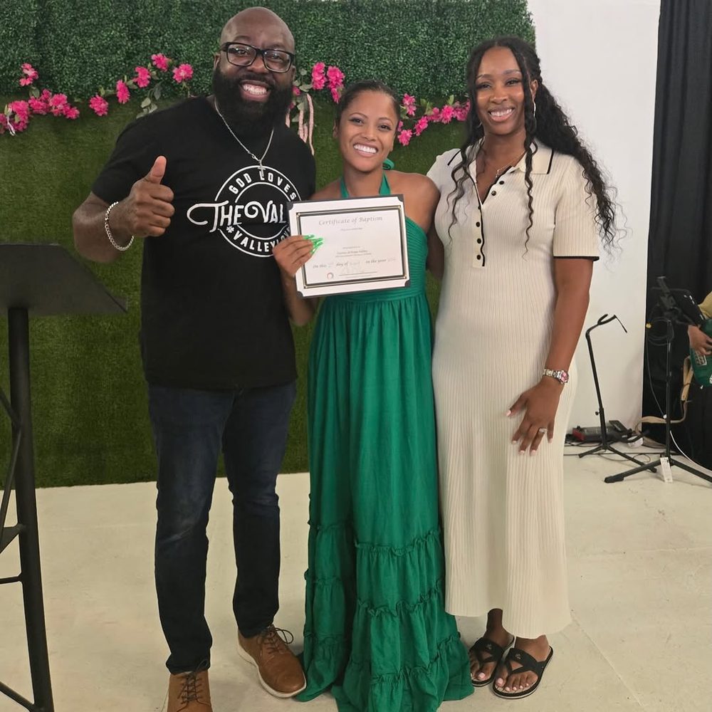 A newly baptized woman holding her baptism certificate, smiling between two church leaders